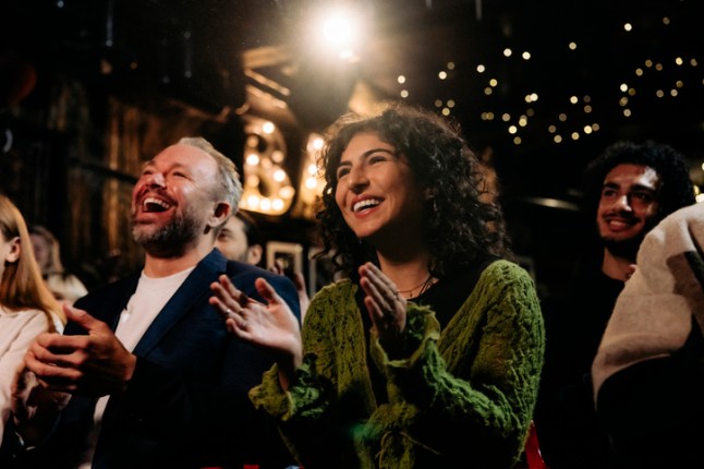 Happy audience laughing and clapping while watching comedy stage show in illuminated theater