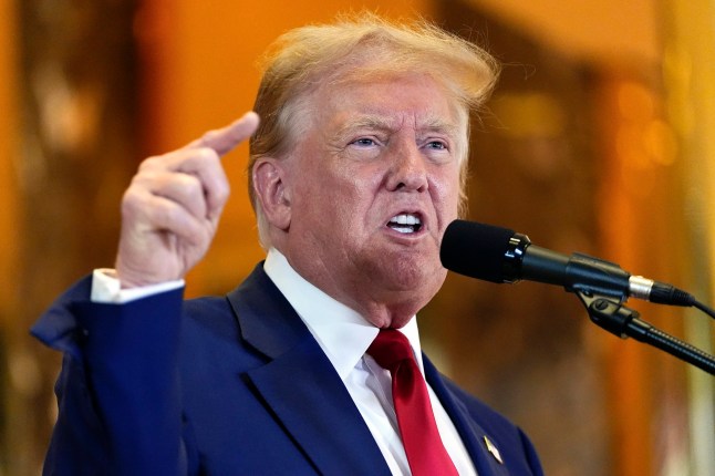 Former president Donald Trump raises his left hand as he speaks into a microphone