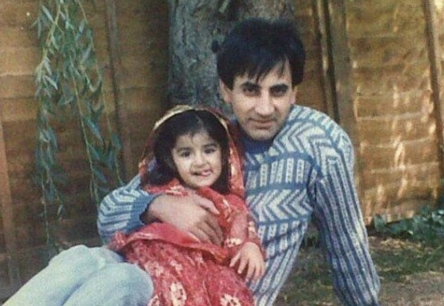 An old photo of Sharan and her dad sitting in the back garen, she is wearing a red dress and he is wearing a blue jumper and jeans