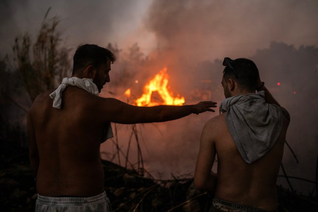 TOPSHOT - Volunteer stand in front of a small pocket of fire as wildfires burn near Penteli, on August 12, 2024. Greece's civil protection authorities ordered the evacuation of several towns in the north-eastern suburbs of Athens, threatened by a violent fire that started the day before and is spreading. European Union said that four countries -- Italy, France, the Czech Republic and Romania -- would send assistance at the request of Greece which is combating a massive wildfire burning through Athens suburbs. (Photo by Angelos TZORTZINIS / AFP) (Photo by ANGELOS TZORTZINIS/AFP via Getty Images)