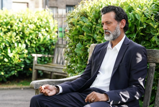 Nish Panesar sitting on a bench in Albert Square in EastEnders