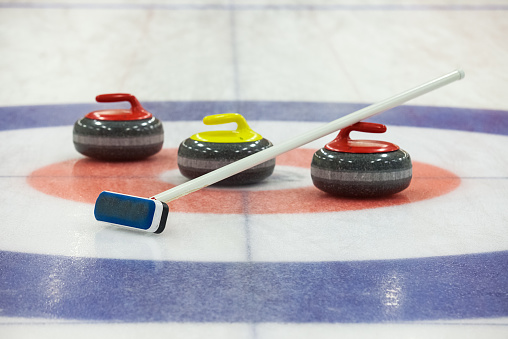 Three curling rocks and a sweeper on ice rink