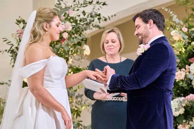 Emma Barnes and Caspar Todd on their wedding day for Married At First Sight. They are exchanging rings. Emma is wearing an off-the-shoulder white gown and Casper has on a wedding suit.