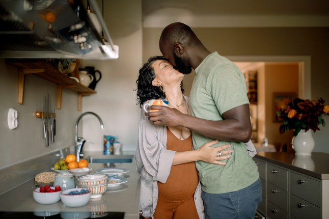 Affectionate pregnant couple kissing while standing in kitchen at home