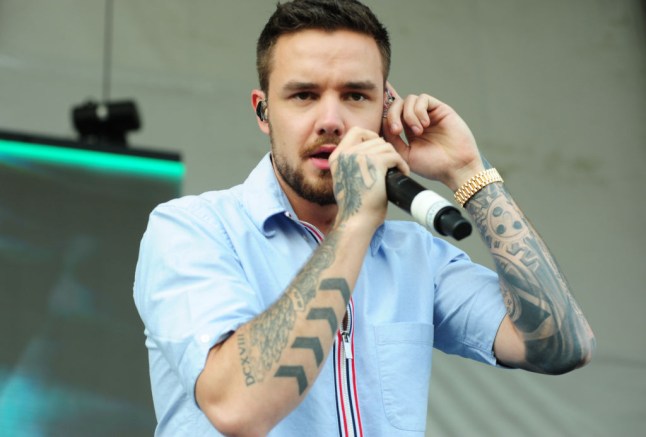 Liam Payne in a blue shirt, singing into a microphone and holding his earpiece