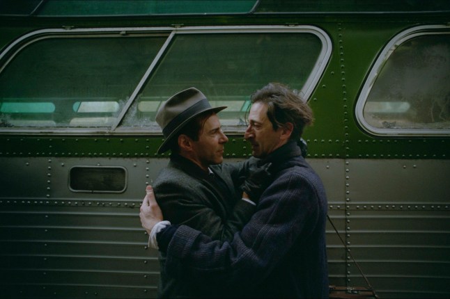 Alessandro Nivola, left, as Attila, and Adrien Brody as Laszlo embrace in front of a bus in a scene from The Brutalist