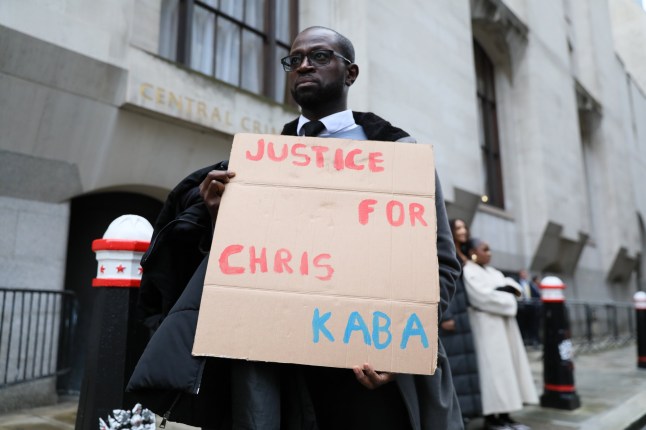 LONDON, ENGLAND - OCTOBER 2: A protester in support of Chris Kaba holds a banner outside the Old Bailey before the trial of a Met Police officer being tried for his murder, on October 2, 2024 in London, England. Chris Kaba, 24, was shot dead by Met Police Officer, Martyn Blake, after a police pursuit of his car ended in Streatham Hill on the night of September 5, 2022. No firearms were found at the scene. In an Independent Office for Police Conduct (IOPC) investigation Blake was charged with murder. (Photo by Alishia Abodunde/Getty Images)