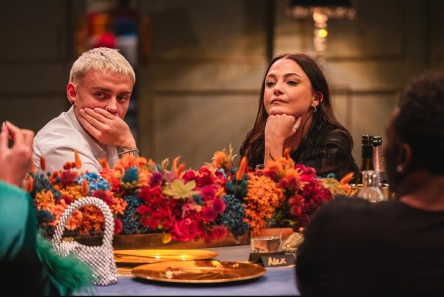 Married At First Sight UK Eve Reid and Charlie Curtis sat at a dinner table looking tense. They both are leaning on their hands. The table is decorated with autumnal flowers.