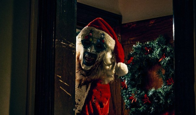 A still from Terrifier 3 of Art the Clown with bloodon his face wearing a Santa costume peering around the door