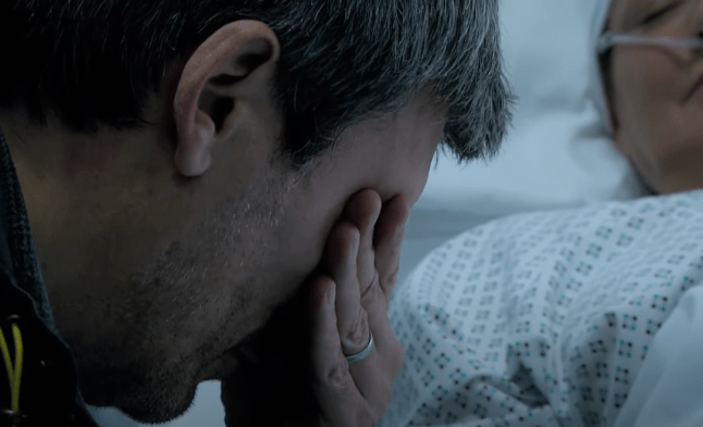 Cain Dingle with his head in his hands next to Moira in her hospital bed in Emmerdale