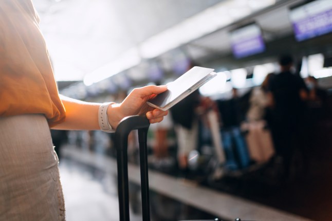 Cropped shot of woman's hand holding passport and suitcase while waiting in line for the check-in counter at airport terminal. Ready for a trip. Business travel. Travel and vacation concept