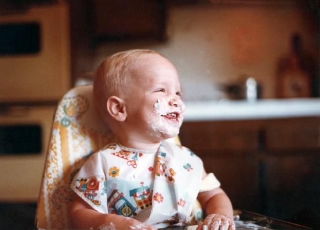 Smiling one year old baby boy with his face covered in cake and icing on his very first birthday.