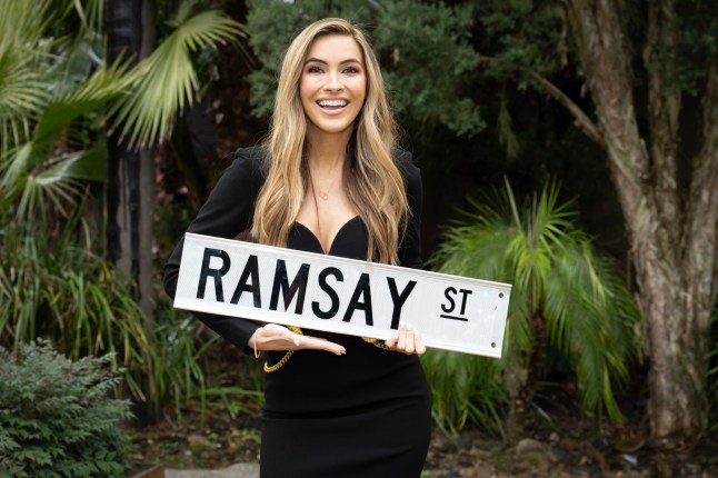 Chrishell Stause holds a Ramsay Street sign