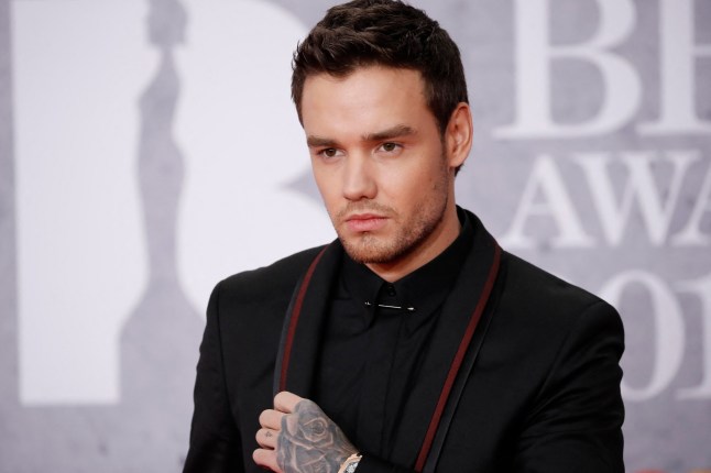 Liam Payne poses on the red carpet for Brit Awards in black suit with red edge.