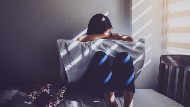 A young woman in a room leaning onto a pillow upset.