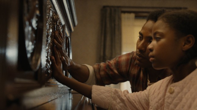 A still from The Piano Lesson in which John David Washington is looking at a piano and touching it with his niece