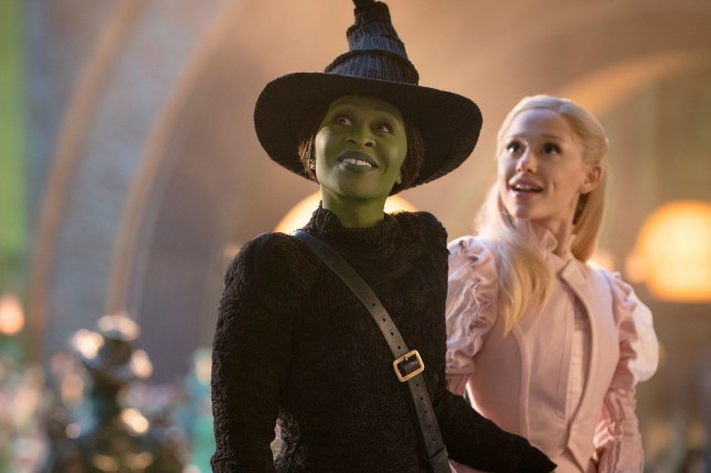 Cynthia Erivo as Elphaba with green skin and in a black outfit and pointed witch's hat, left, and Ariana Grande as Glinda in pink in a scene from the film Wicked