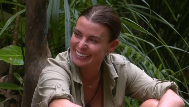 A still of Coleen Rooney in a green-grey top, smiling