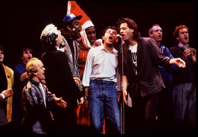 LONDON, ENGLAND - APRIL: The assembled cast of Comic Relief Live, a live comedy show presented on the evenings of 4th, 5th & 6th of April 1986 at the Shaftesbury Theatre in London's West End, perform the Band Aid single "Do They Know it's Christmas". Left to right, Nigel Planer, Graham Chapman, Bob Geldof, Frank Bruno, Lenny Henry, Ben Elton, Christopher Ryan (back), David Rappaport and Dawn French on April 1986 in London, England. (Photo by Comic Relief/Comic Relief via Getty Images)1