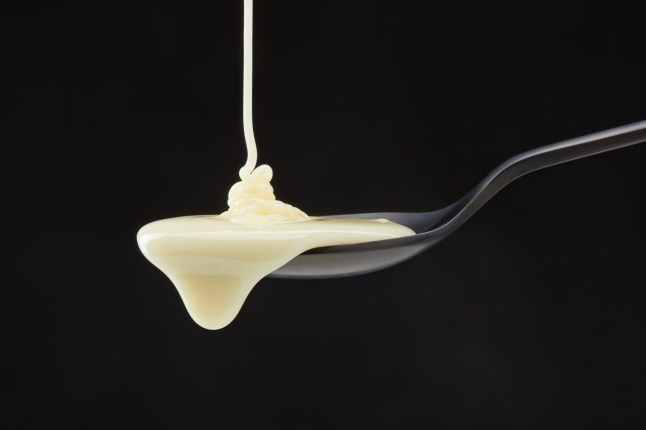 Condensed milk pouring down from black spoon against a black background. Cream in a spoon.