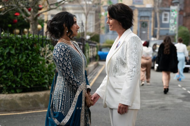 Suki Panesar and Eve Unwin holding hands and gazing lovingly at each other in Albert Square at their wedding in EastEnders