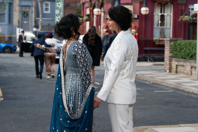 Suki Panesar and Eve Unwin holding hands and gazing lovingly at each other in Albert Square at their wedding in EastEnders