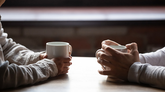 Close up woman and man holding cups of coffee on table