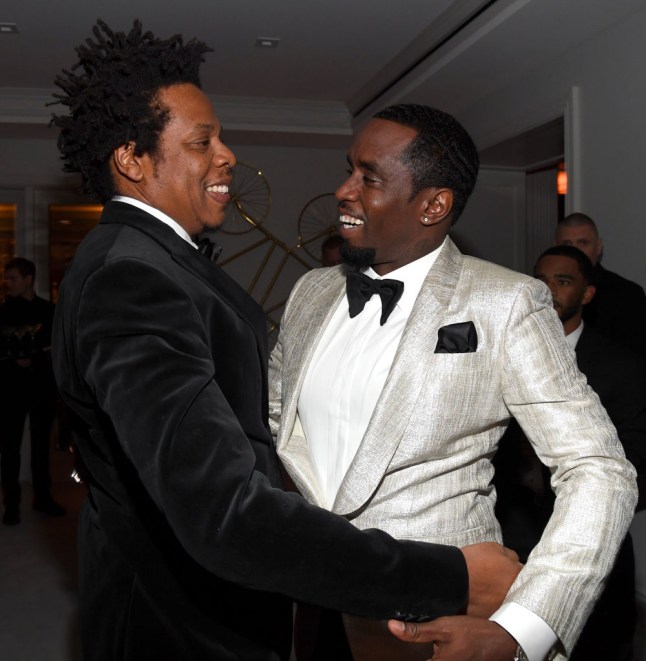 Diddy in shiny suit and jay Z in black suit as they hug and grin at each other