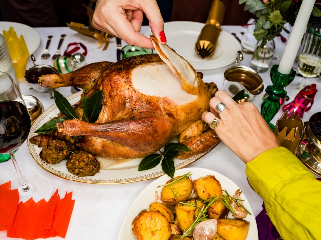 Close up friends carving roasted turkey at Christmas dinner table