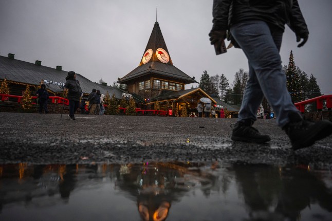 A tourist walks over a rain puddle during a visit to the Santa Claus Village near Rovaniemi, Finnish Lapland, on November 16, 2024. With a month to go until Christmas, Santa Claus is busy preparing, but the warming climate and lack of snow in his Arctic hometown have him worried. By this time of year, the town of Rovaniemi in Finnish Lapland -- marketed by tourism officials since the 1980s as the "real" home of Santa Claus -- should be white and pretty. (Photo by Jonathan NACKSTRAND / AFP) (Photo by JONATHAN NACKSTRAND/AFP via Getty Images)