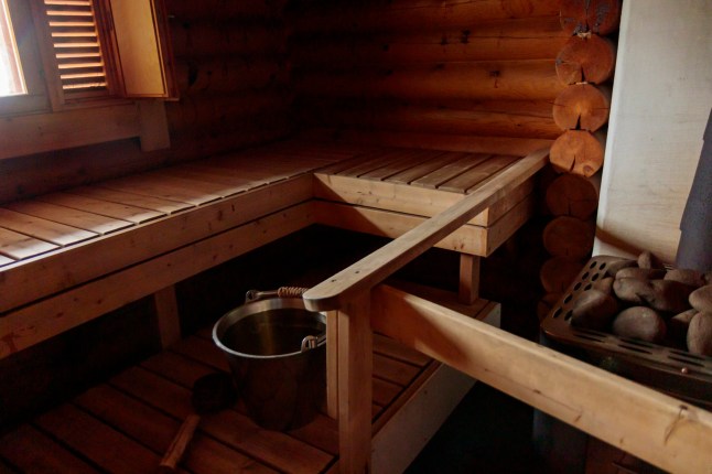 Finnish traditional wood sauna, accessory in steam room, sauna heater with stones, metal stainless steel bucket and old ladle, banner with copy space.