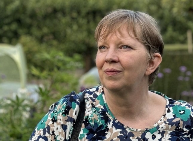 Clare in a garden, wearing a flowery dress, looking off to the distance