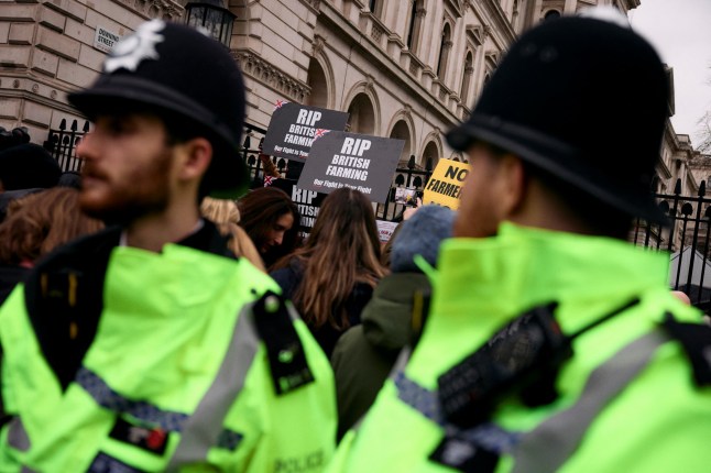 Demonstrators hold placards reading "RIP British Farming" as they stand behind police officers and in front of Downing Street gates, during a stop "the death of British Farming" demonstration, to protest against changes to inheritance tax rules for land ownership for farmers, in central London, on December 11, 2024. (Photo by BENJAMIN CREMEL / AFP) (Photo by BENJAMIN CREMEL/AFP via Getty Images)