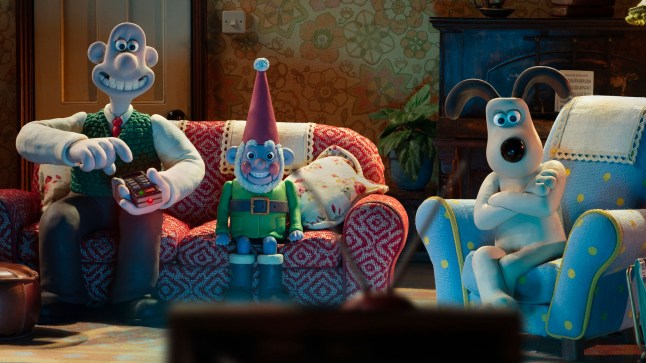 Wallace, Norbot and Gromit sit on the sofa in the living room watching TV in Wallace & Gromit: Vengeance Most Fowl