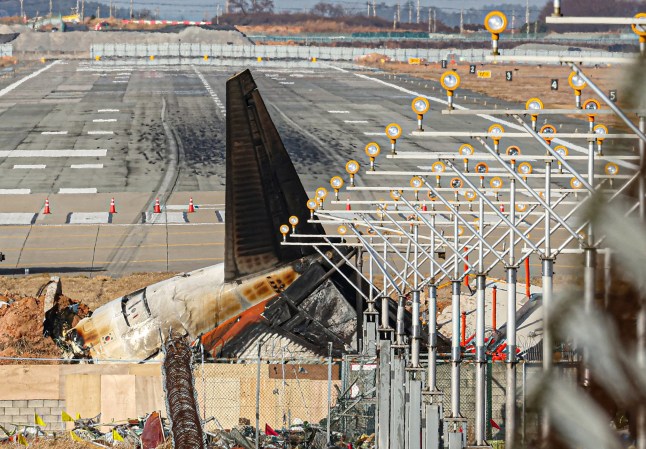 The wrecked tail section of the Jeju Air Boeing 737-800 aircraft that crashed and burst into flames is seen at the end of the runway at Muan International Airport in Muan, some 288 kilometres southwest of Seoul on December 30, 2024. The Boeing 737-800 was carrying 181 people from Thailand to South Korea when it crashed on arrival on December 29, killing everyone aboard -- save two flight attendants pulled from the twisted wreckage of the worst aviation disaster on South Korean soil. (Photo by YONHAP / AFP) / - South Korea OUT / RESTRICTED TO SUBSCRIPTION USE - NO ARCHIVES (Photo by -/YONHAP/AFP via Getty Images)