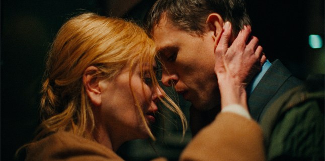 Nicole Kidman as Romy in a camel-coloured overcoat wraps her hands around the nape of and touches her forehead to Harris Dickinson's as Samuel, in a blue shirt and grey suit in a scene from Babygirl