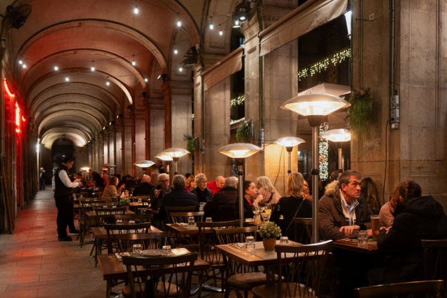 Tourists sit on a restaurant terrace as they shelter from the cold with gas heaters