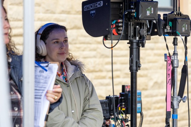 Dani Harmer has headphones on as she looks through camera lens on film set