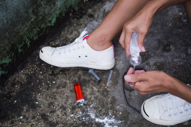 Close up hand holding old spoon with Ketamine, cigarette lighter, syringe on dirty cement floor. Addictive substance, narcotic, habit-forming substance concept.