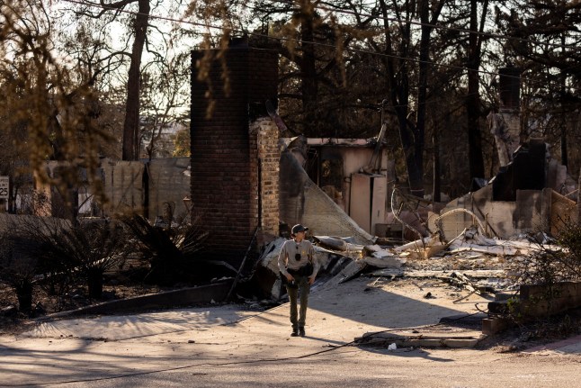 A sheriff's deputy walks among the remains of a house reduced to rubble by the Eaton Fire during search and rescue operations in Altadena, California, on January 13, 2025. Search teams looking for people killed in devastating Los Angeles blazes moved from house to house, as firefighters girded for hurricane-force winds that could spark further flare-ups. With the disaster in America's second biggest city in its seventh day, 24 people are known to have died, with the toll expected to rise, and more than 90,000 people are still displaced. (Photo by ETIENNE LAURENT / AFP) (Photo by ETIENNE LAURENT/AFP via Getty Images)