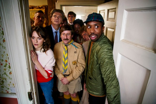 Charlotte Ritchie as Alison, Ben Willbond as Captain, Simon Farnaby as Julian, Jim Howick as Pat, Katy Wix as Mary, Mat Baynton as Thomasm Lolly Adefope as Kitty, Laurence Rickard as Robin and Keill Smith-Bynoe as Mike peering through a door frame in BBC show Ghosts