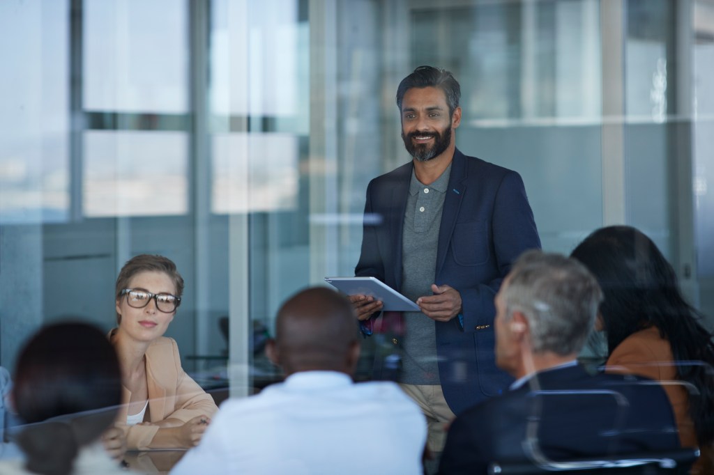 Business people dressed casual/corporate, talking together in large glass conference room