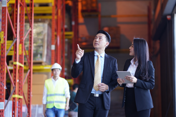 Two business people walking in the warehouse using tablet check product storage and shipping for sorting before shipping