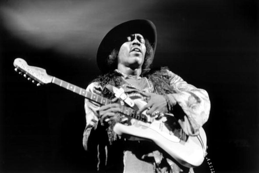 Jimi Hendrix performing live onstage in 1968, playing a white Fender Stratocaster guitar.