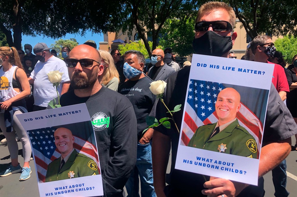 Men hold signs outside of the Santa Cruz County Sheriff-Coroner's Office to pay respects in the death of Sergeant Damon Gutzwiller. 