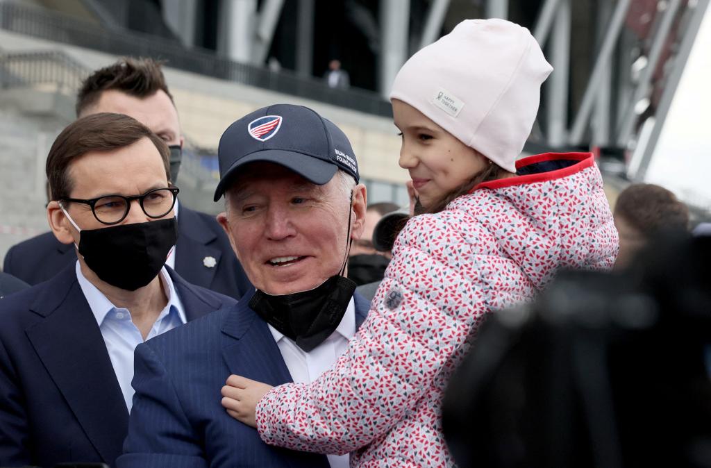 U.S. President Joe Biden, flanked by Polish Prime MInister Mateusz Morawiecki, holds a child as he visits Ukrainian refugees at the PGE National Stadium, in Warsaw, Poland March 26, 2022.