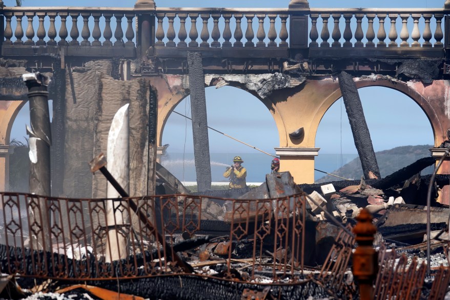 A firefighter hoses down hot spots from a beachfront home in the aftermath of the Coastal Fire.