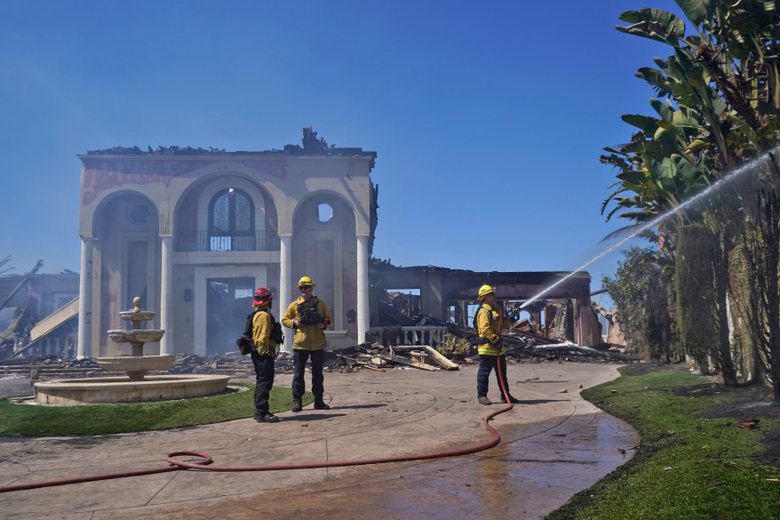 Members of the Torrance Fire Department protect the remains of a fire-damaged home in the aftermath of the Coastal Fire.