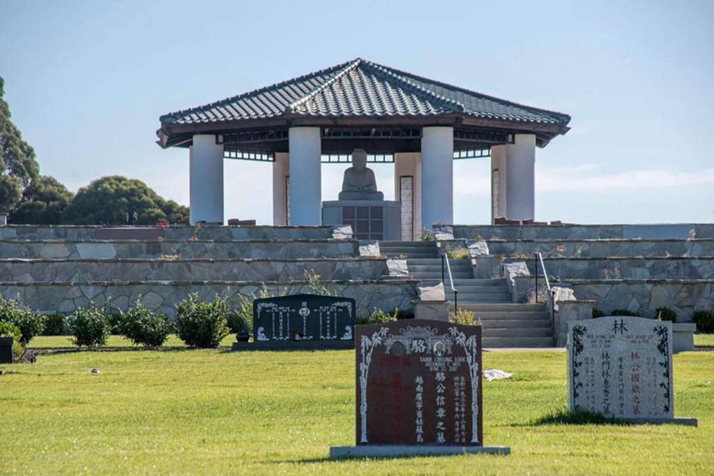 Gravestones are in the forefront of stairs leading up to a monument of Gautama Buddha.