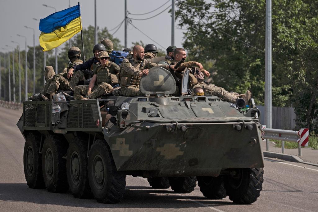 Ukrainian servicemen ride atop of an armored vehicle.